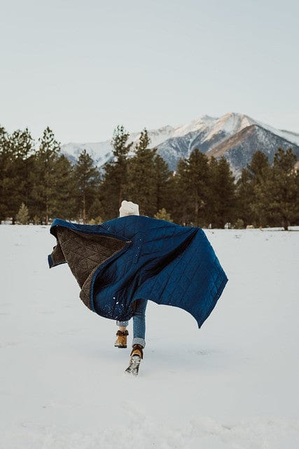 Person running in snow with an ultra-plush fleece, outdoor, Kammok Mountain Blanket, in midnight blue.