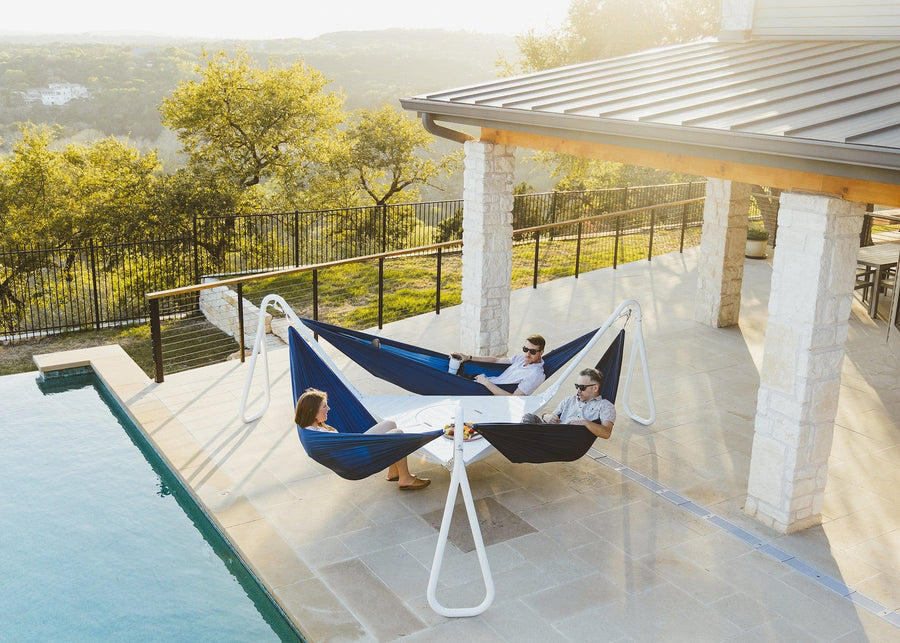 Three people sitting in Hammocks i nfront of a pool in a Kammok Stand Baya Cloud White