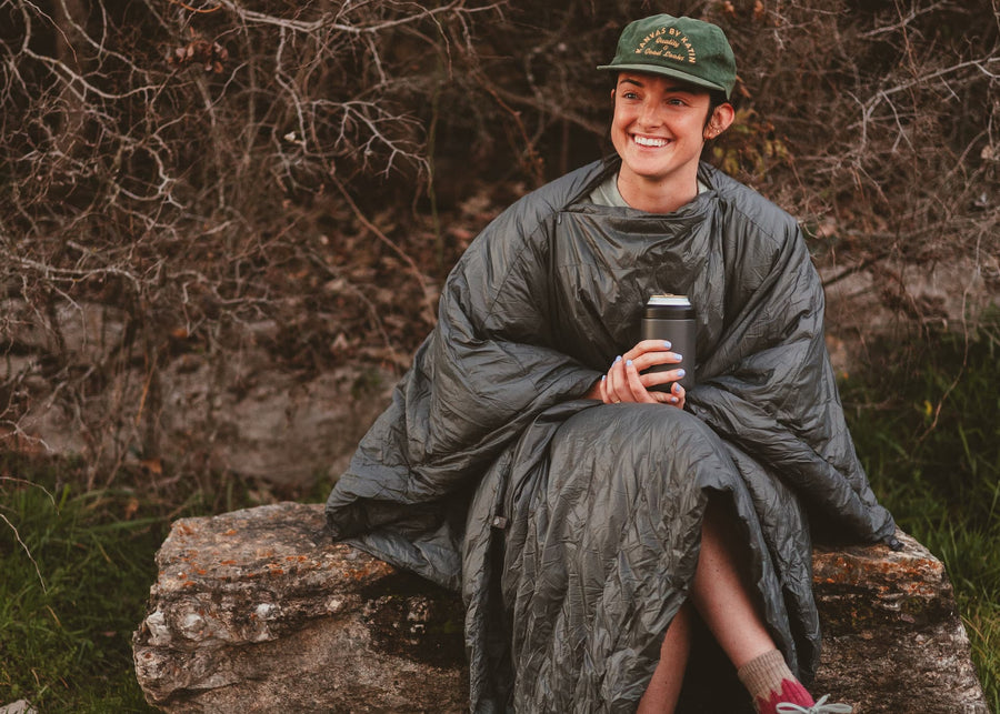 Girl sitting on a rock wearing a Kammok Trail Quilt Firebelly 30°F in Poncho Mode.