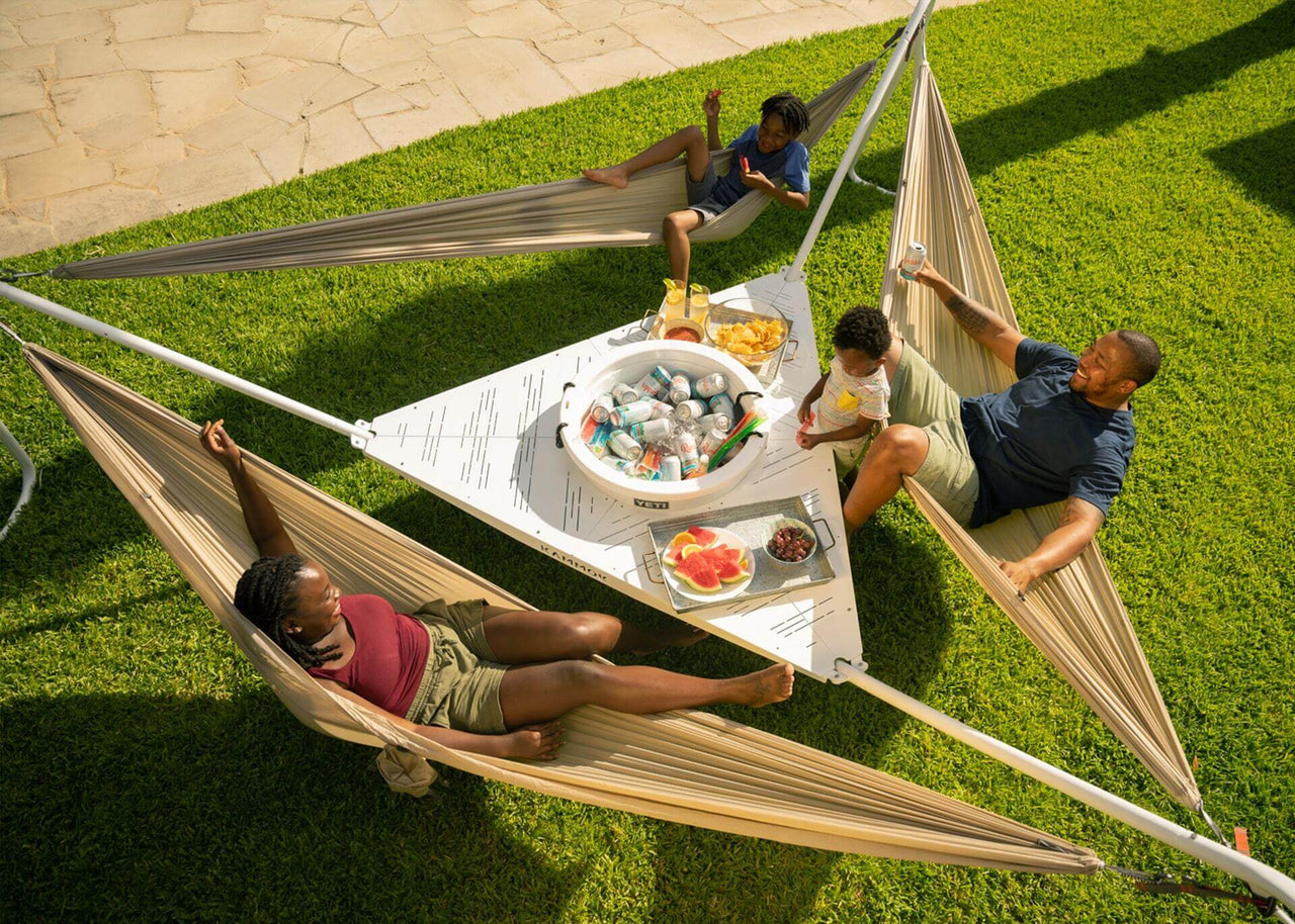 Family sitting in Hammocks around their Kammok Stand Baya 2.0 with food and drinks in the center.