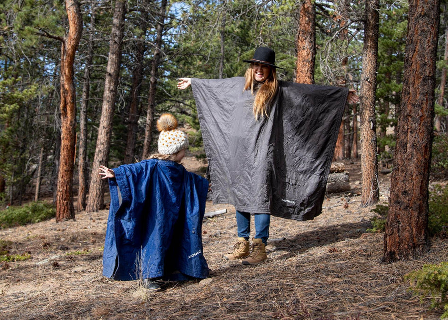 Mom and girl with arms outstretched in the woods wearing their Kammok Blanket Field Blankets.