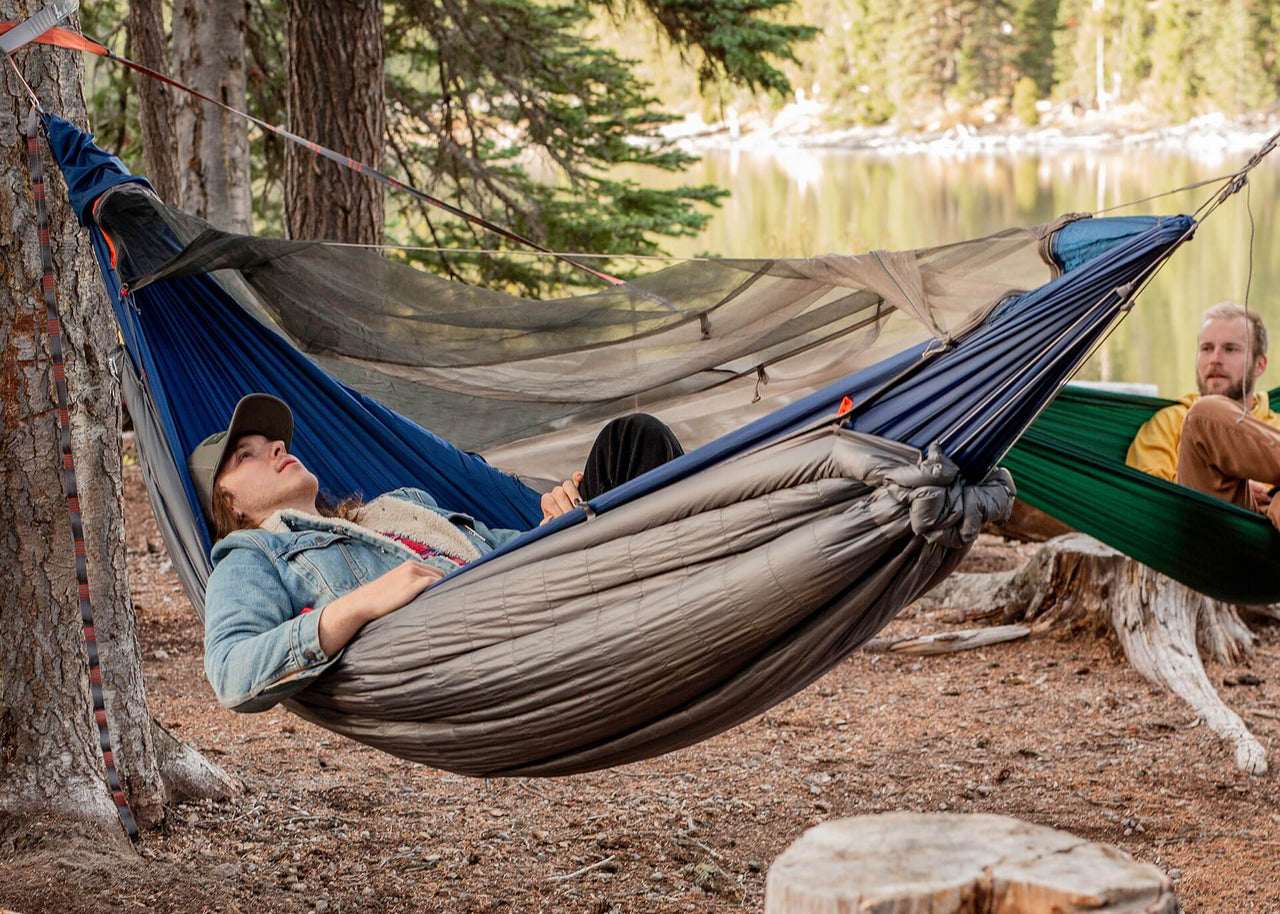 Women lying in hammock next to a river using her FIrebelly as a hammock underquilt.