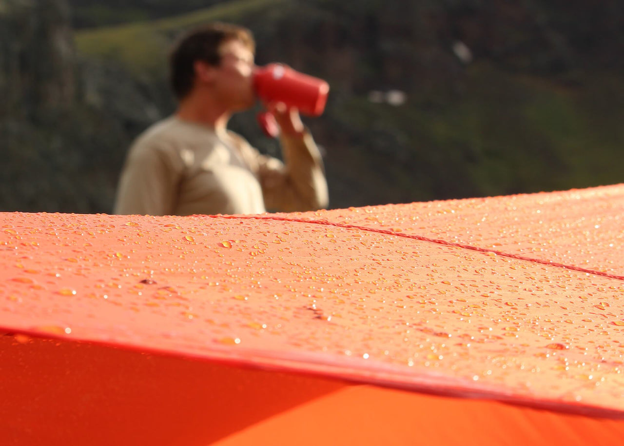 Man drinking next to a Kammok Weather Shelter Kuhli XL