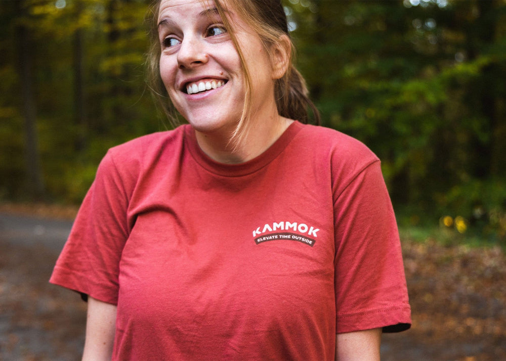 Front side of shirt, women wearing a Kammok Ride in Wonder Tee in red with a graphic of a woolly bear caterpillar and text Ride in Wonder.