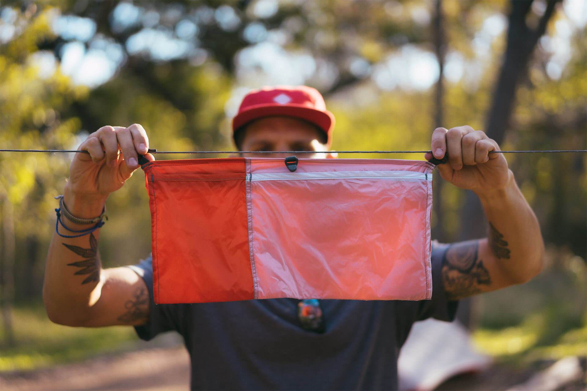 Man with tatoos holding a hammock Ridge Line Organizer in the woods.