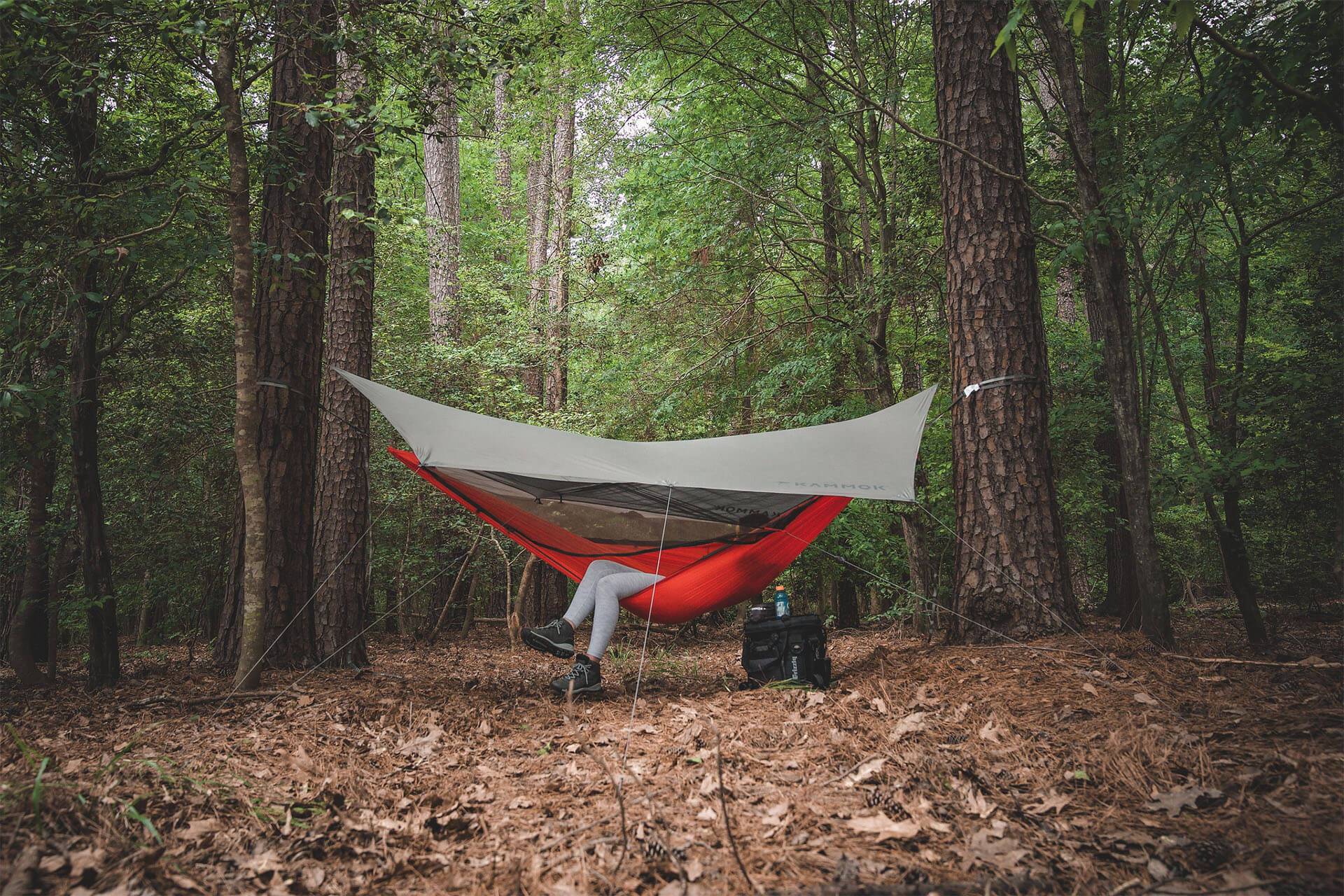 A Hammock Quilt under a shelter between two trees with legs hanging out of hammock.