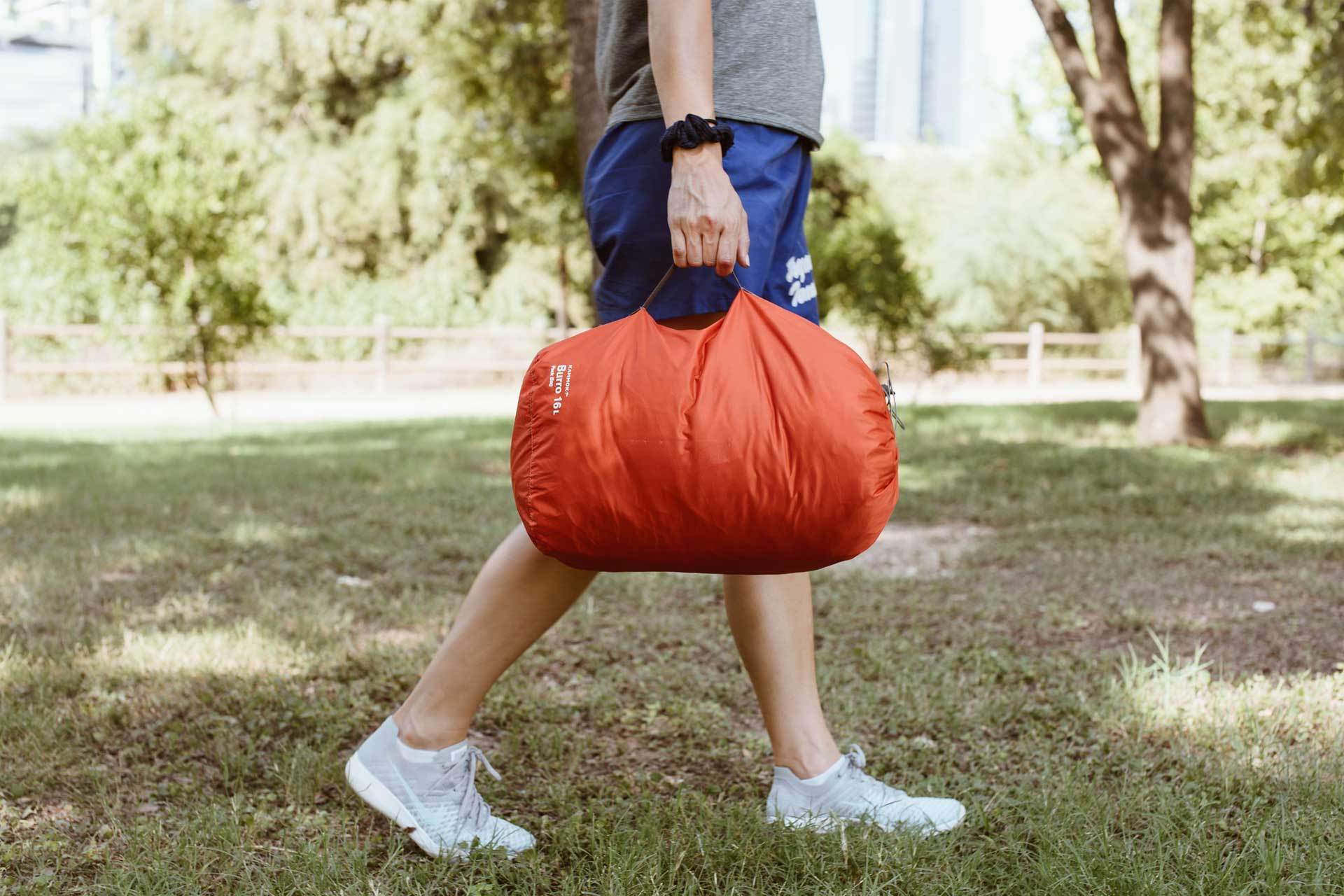 A man walking through grass holding a storage bag.