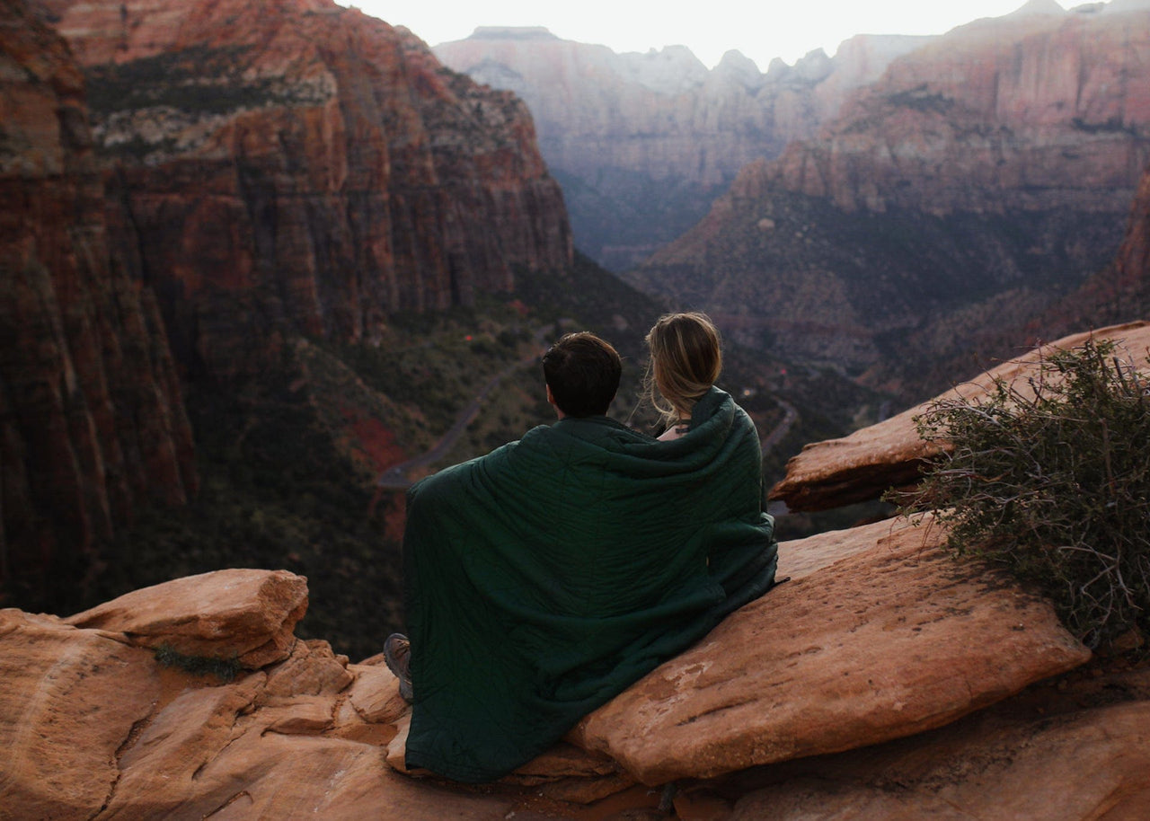 Couple sitting on mountain wrapped in a Kammok Field Blanket overlooking the canyon.