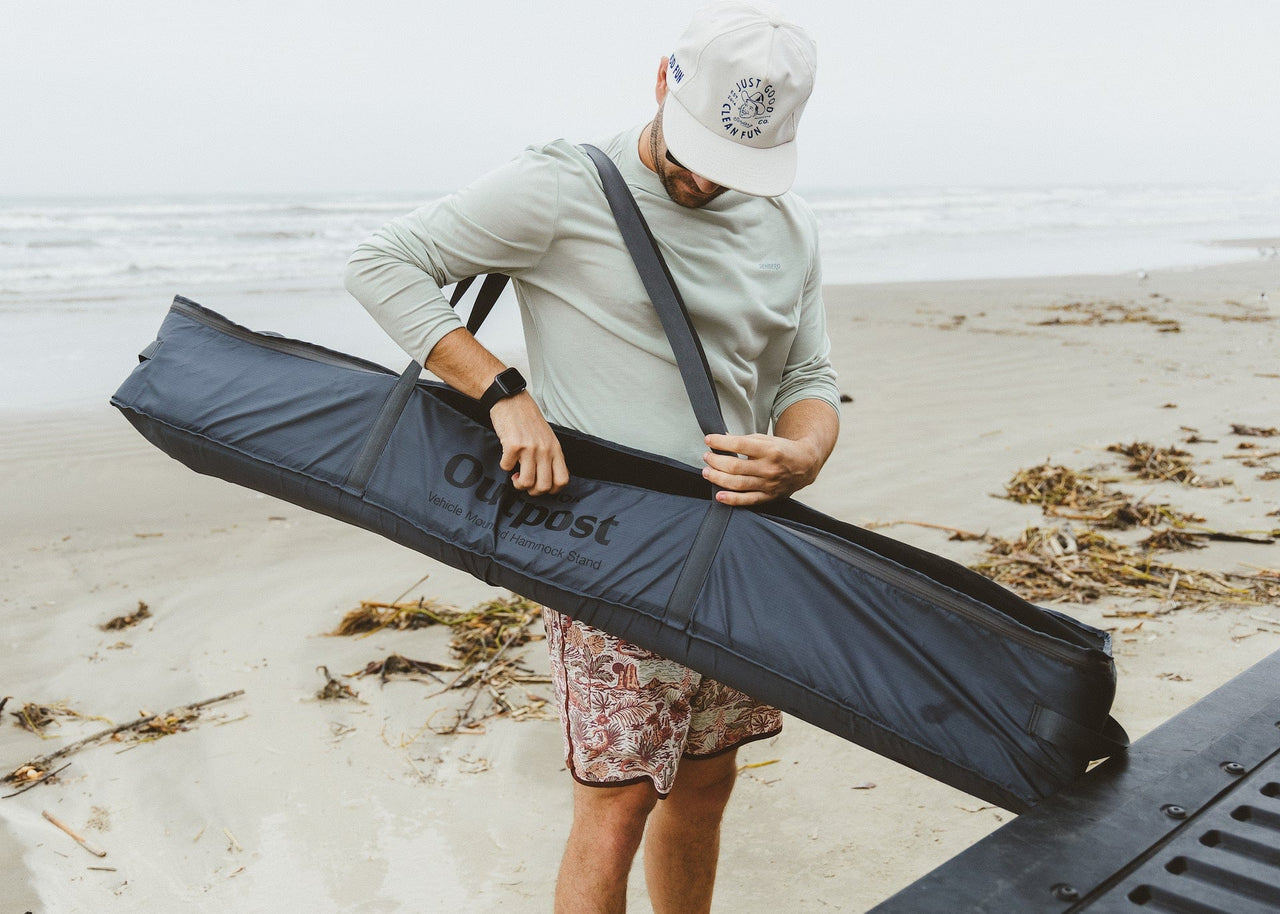 Man carrying his Kammok Outpost in the storage bagon his shoulder on the beach.