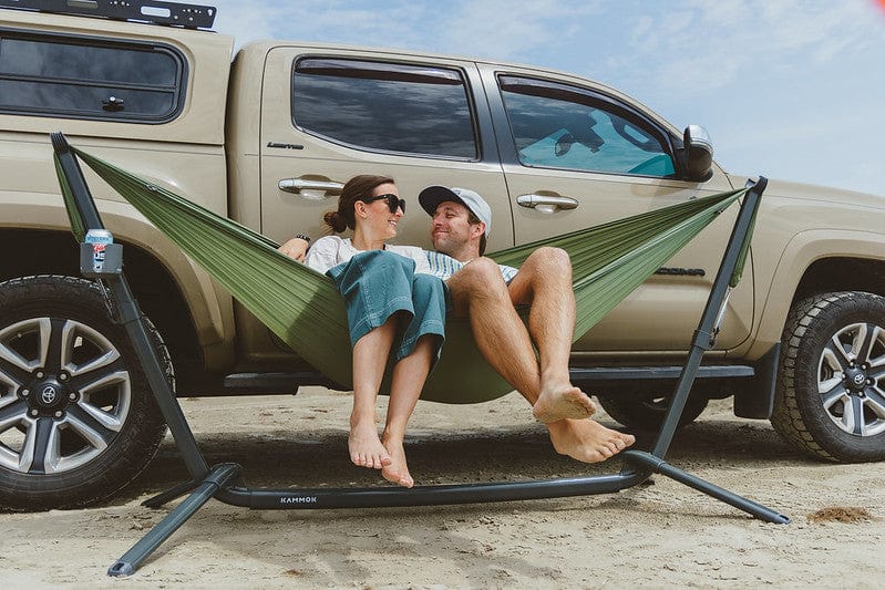 Couple lounging next to their Toyota Tacoma in their Kammok Bundle Swiftlet Hammock Stand Bundle