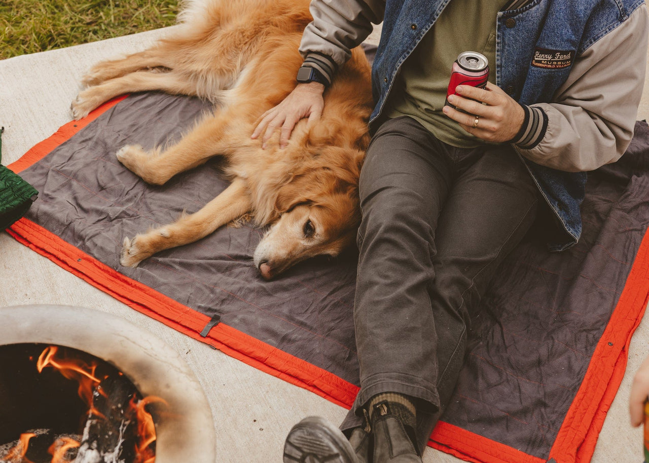 Dog lying on a Kammok Field Blanket next to man's legs.