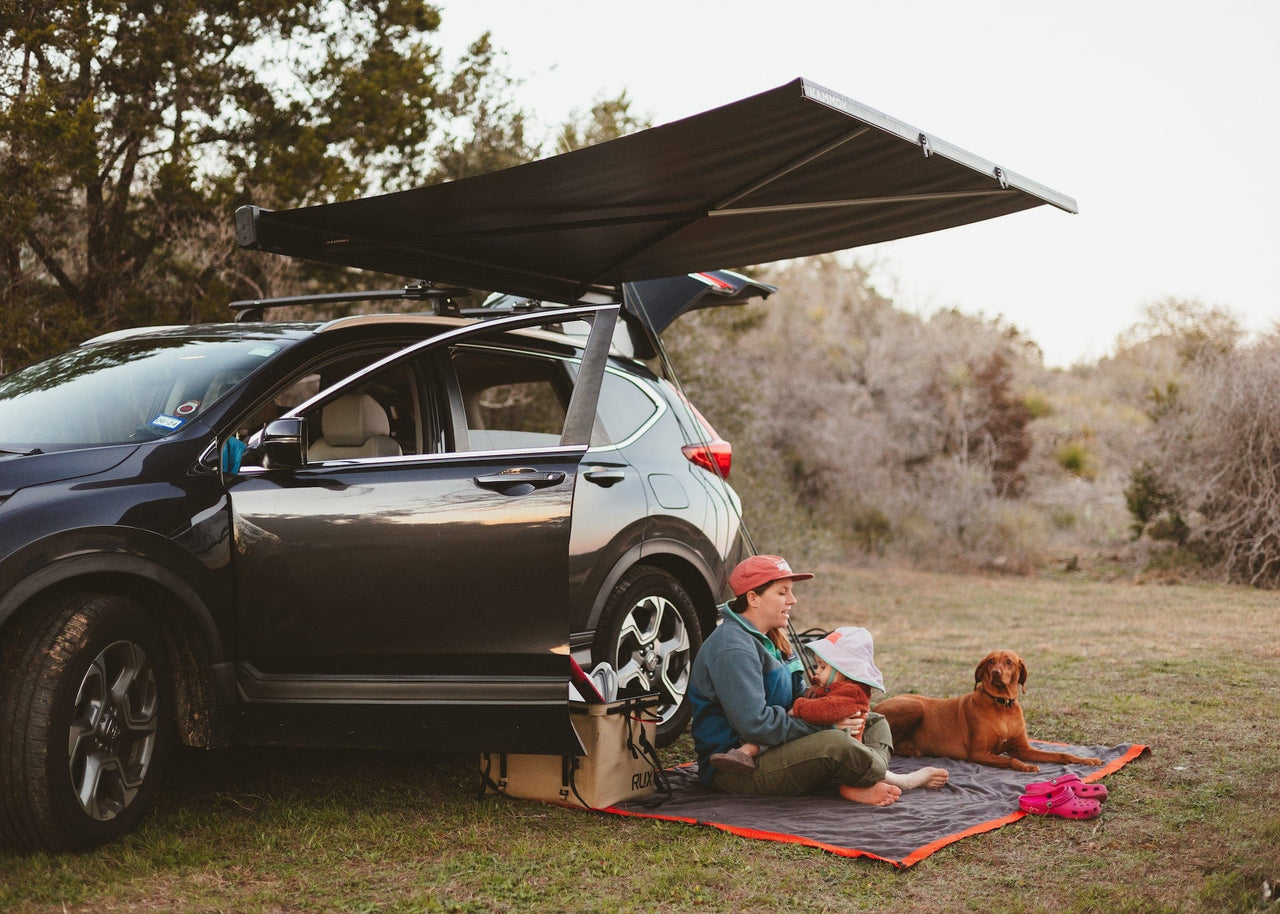 Famiy and dog sitting outside in the woods under the shelter from a Crosswing awning. Completely Customizable  Endlessly adaptable to your lifestyle, Crosswing features a t-slot rail that runs the full length of the aluminum body—perfect for attaching third-party and future Kammok accessories.