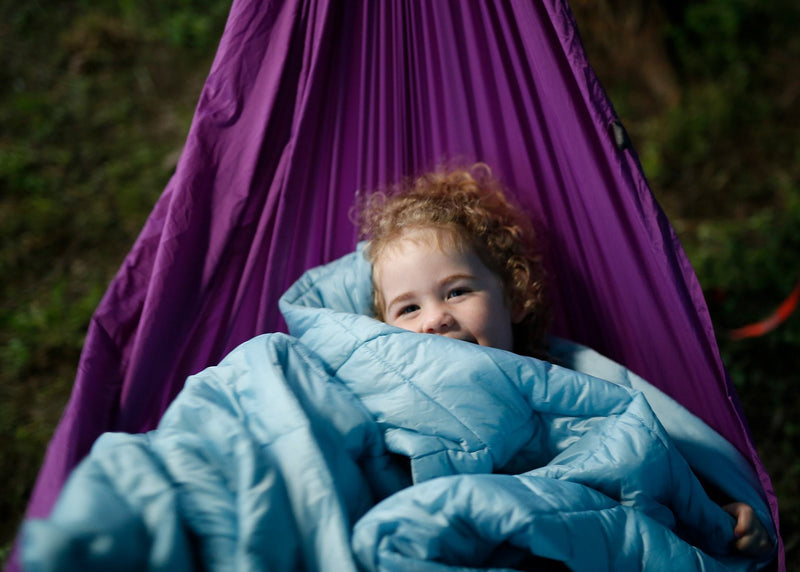 Child curled up in a trail quilt lying in a Kammok Hammock Roo Jr.