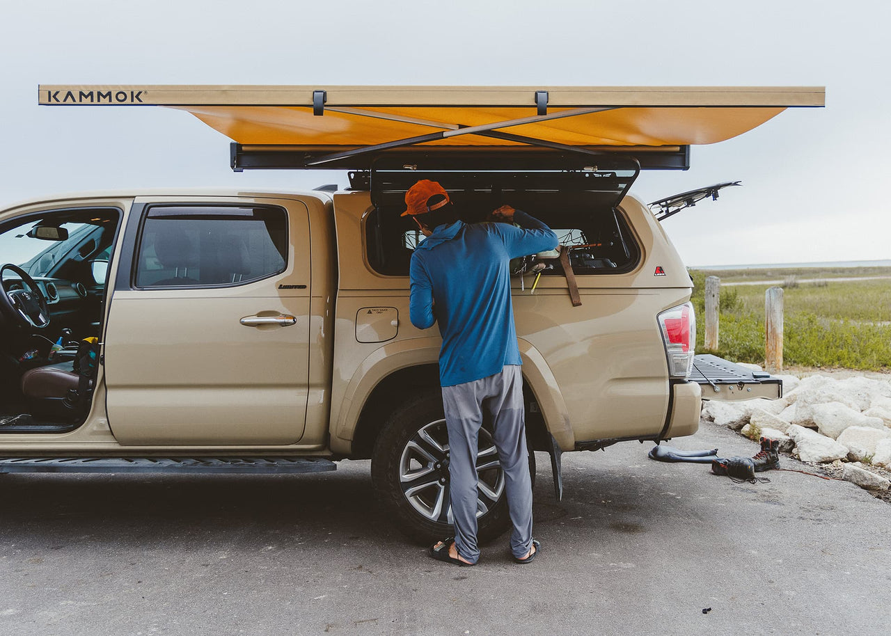 Man standing in a parking lot at his truck under a Crosswing awning grabbing things from his side bed window.