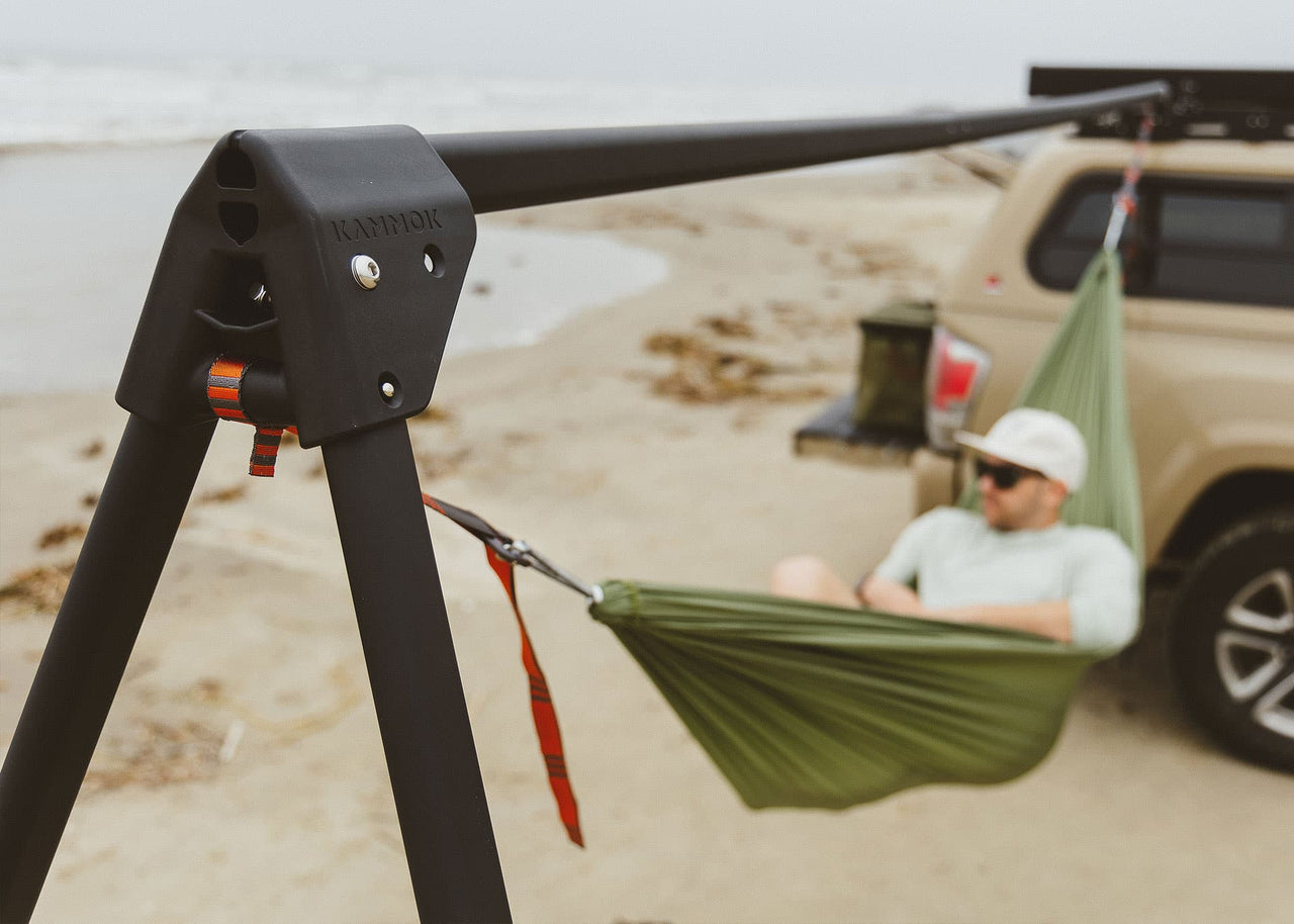 Kammok Stand Outpost installed on an vehicle with man lying in Roo Hammock near the water.