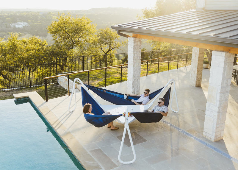 Three people hanging out in the Baya hammock stand next to a pool.