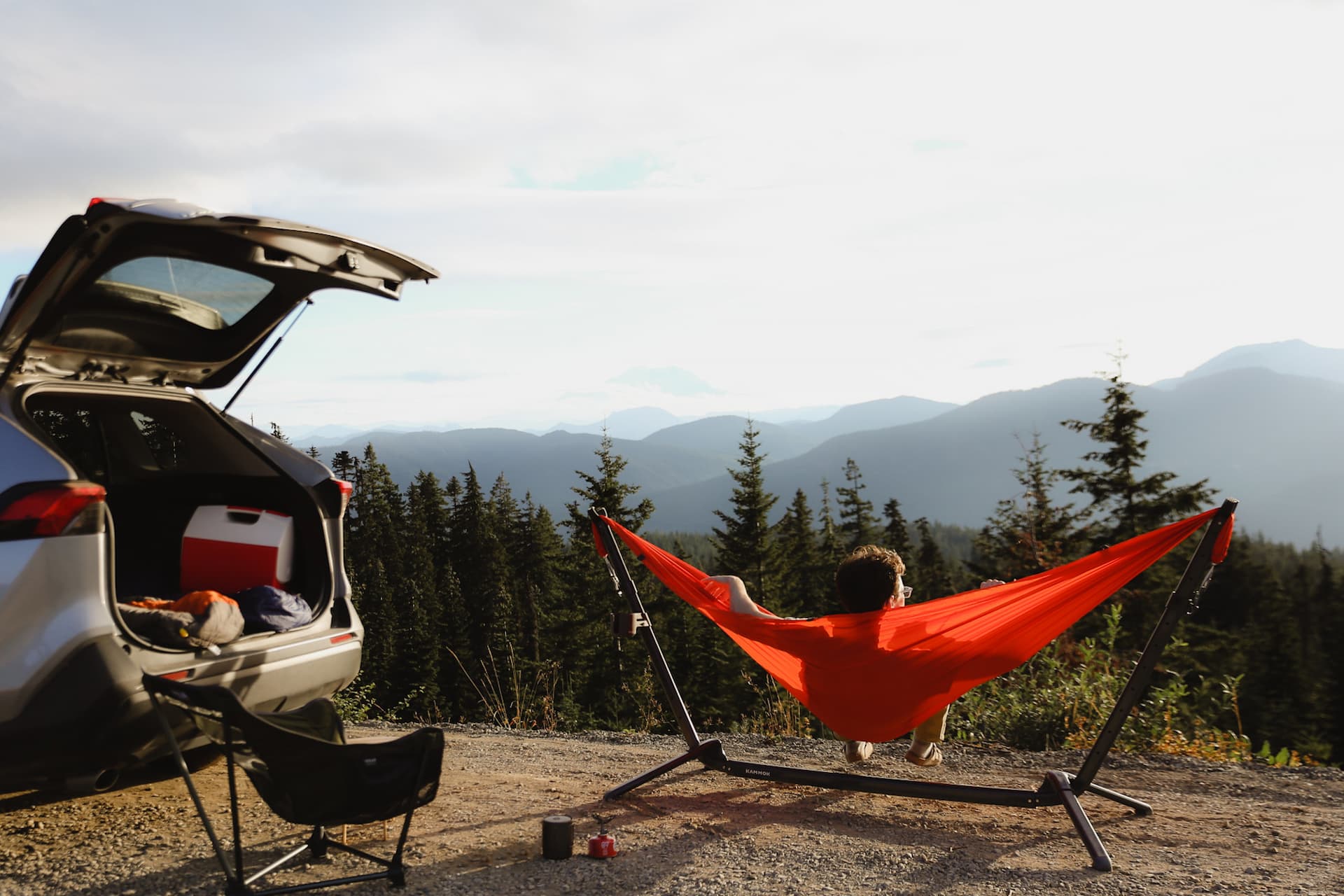 Man lying in a hammock in a Swiftlet Portable Hammock Stand looking out over the mountains behind his car.