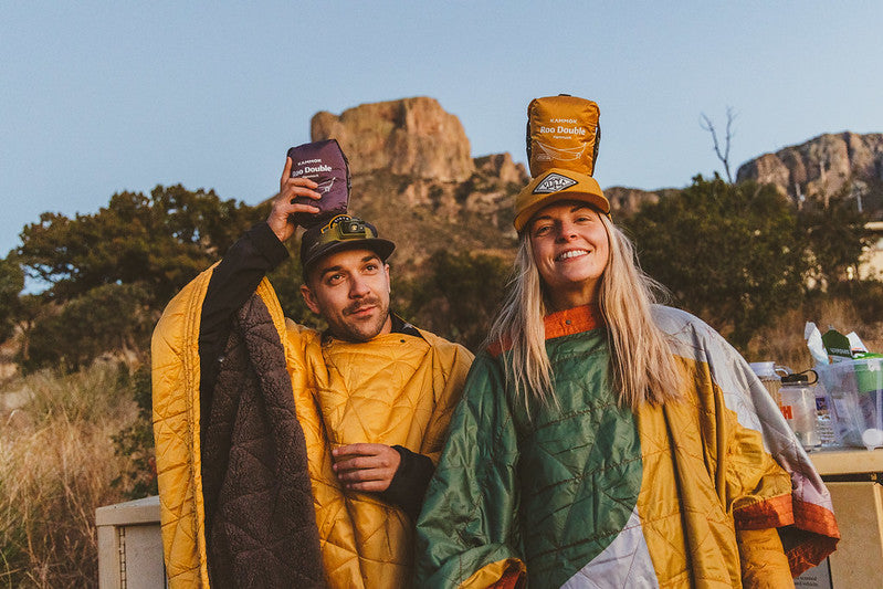 Two friends wearing Kammok poncho blankets while balancing hammocks on their head