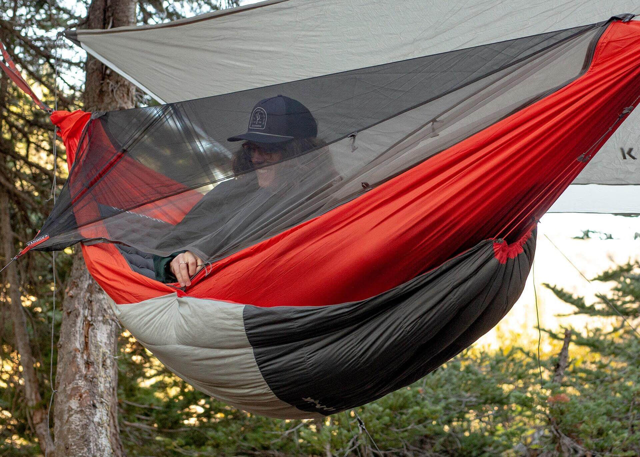 Kammok Trail Quilt Arctos 20°F Crater Gray hanging between two trees with person inside.