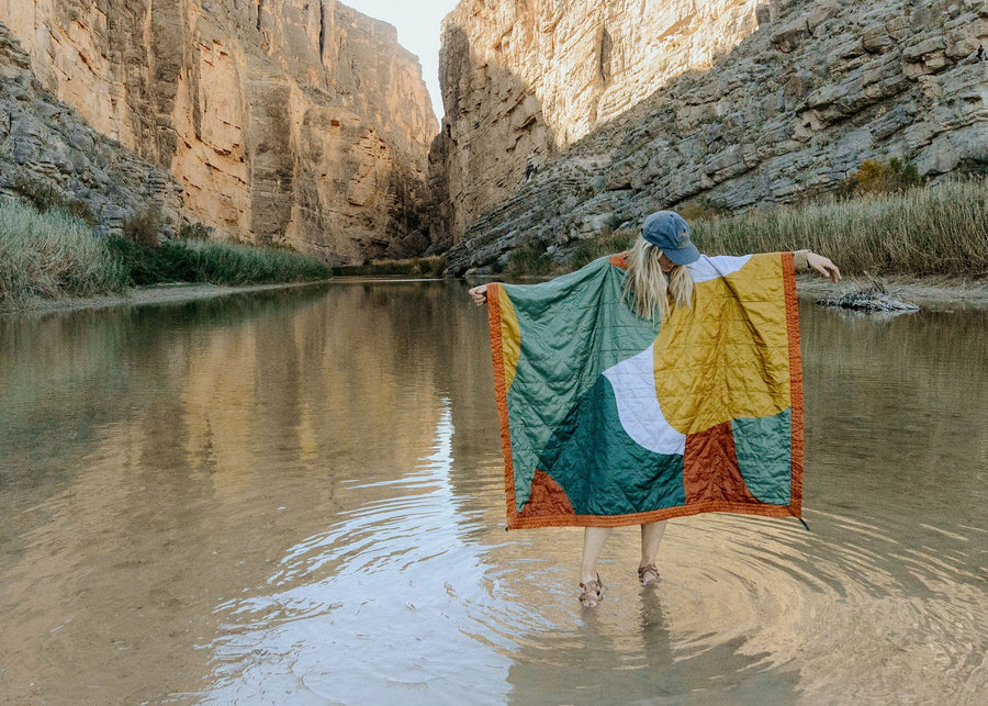 Woman standing in a lake surrounding by mountains wearing a Kammok Blanket Field Blanket Printed