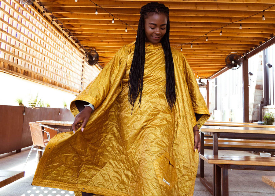 Woman wears a Kammok Field Blanket Printed in mustard yellow and star print pattern, in poncho mode while walking.