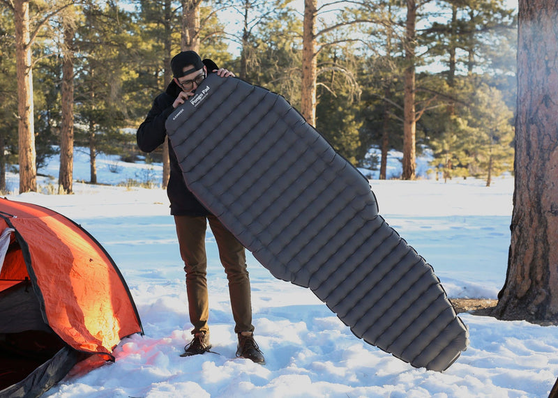 Man blowing up a Kammok Sleep Line Insulated Pongo Pad while standing in snow i woods.