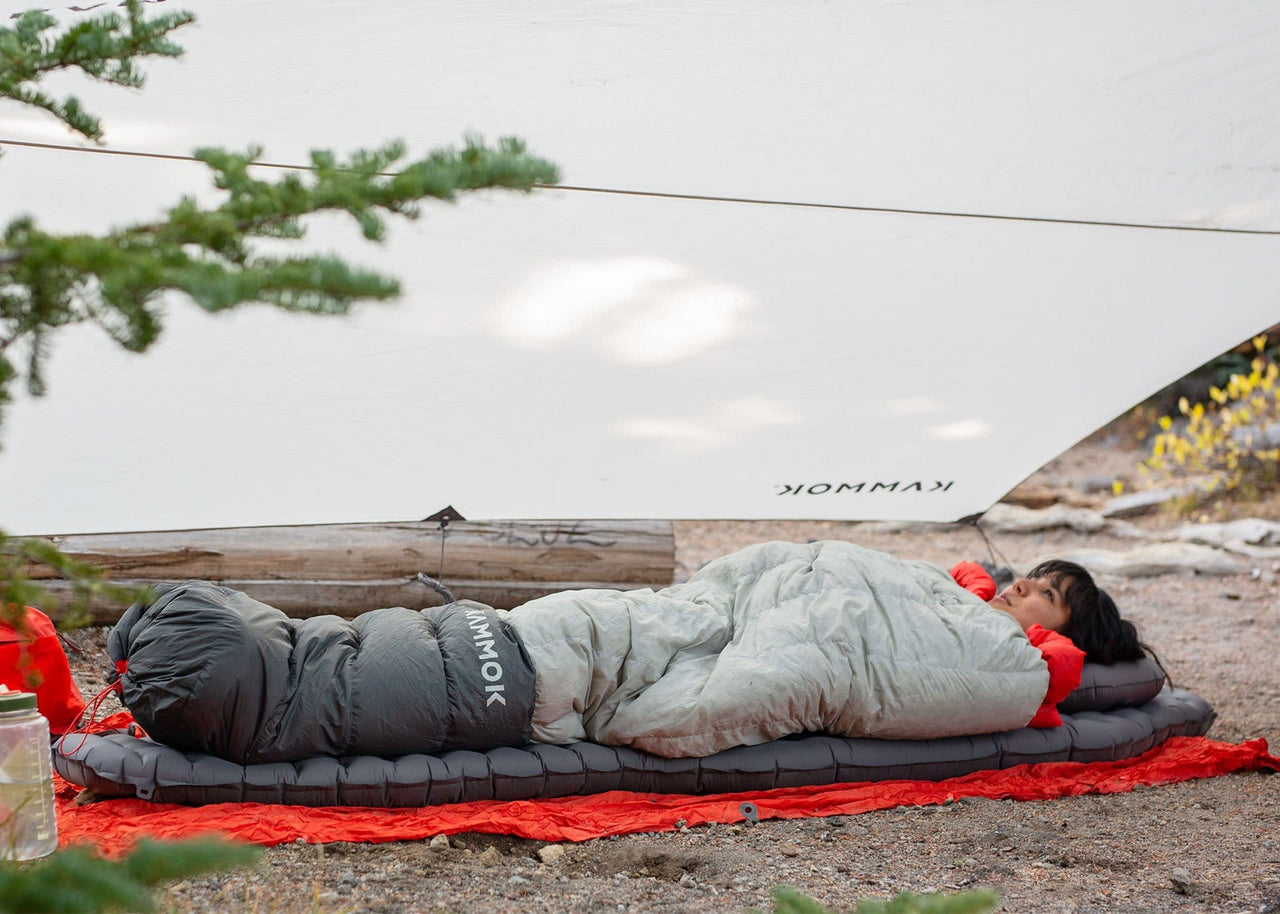 Woman lying on ground on Kammok Sleep Line Insulated Pongo Pad under shelter.