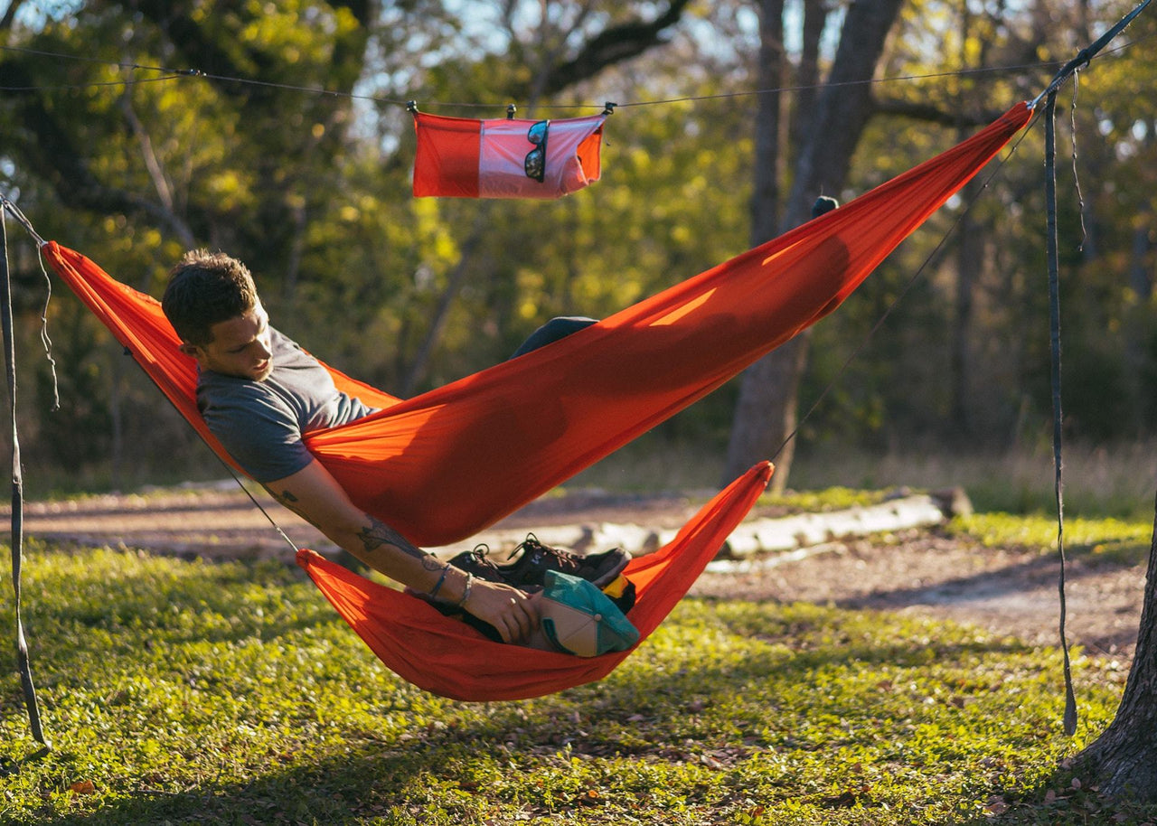 Man in the woods lying on a hammock reaching into his Kammok Storage Joey Gear Sling