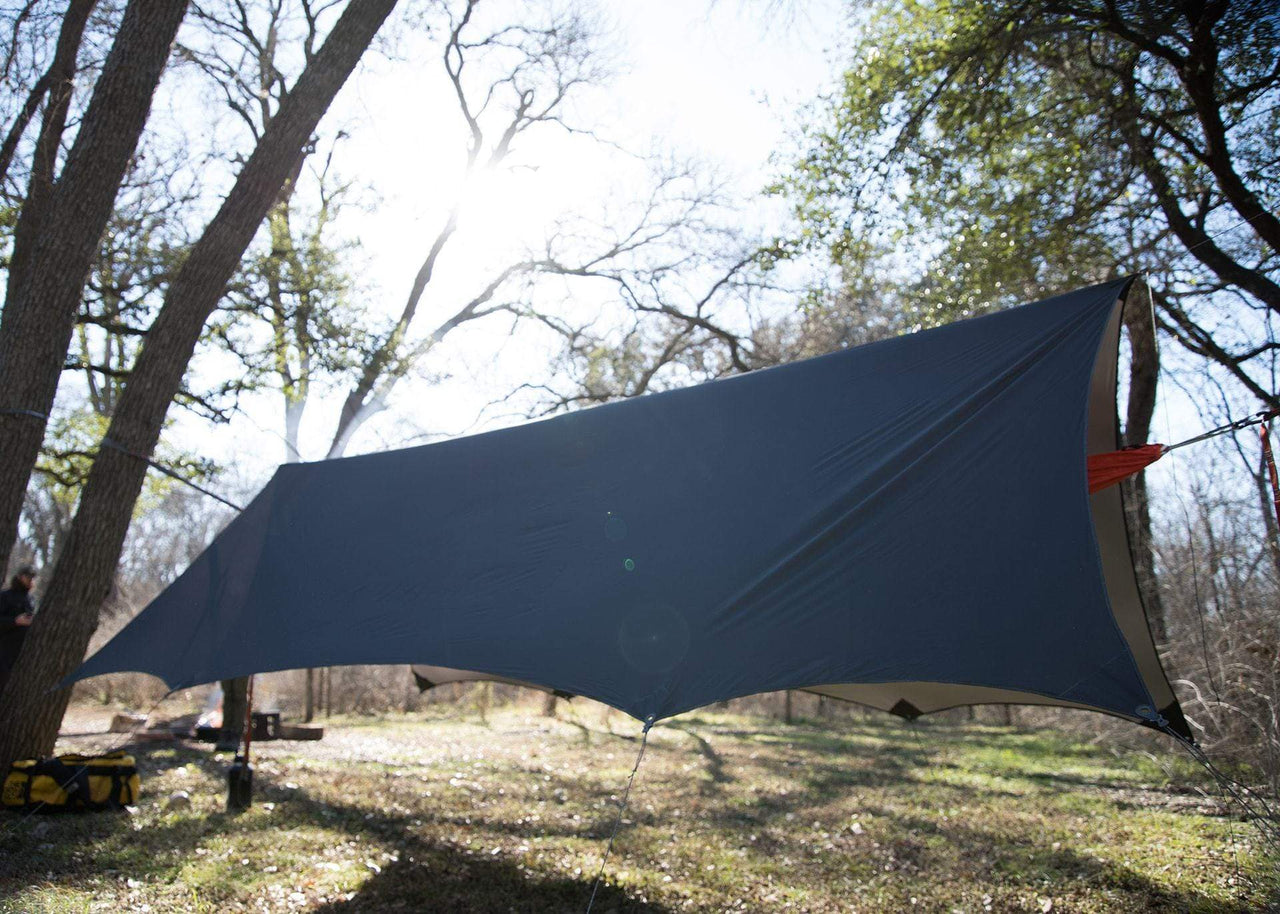 Kammok Weather Shelter Kuhli Pro h anging between two trees at a campsite.