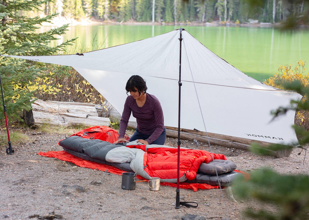 Women underneath a Kuhli weather shelter setting up a sleeping bag.