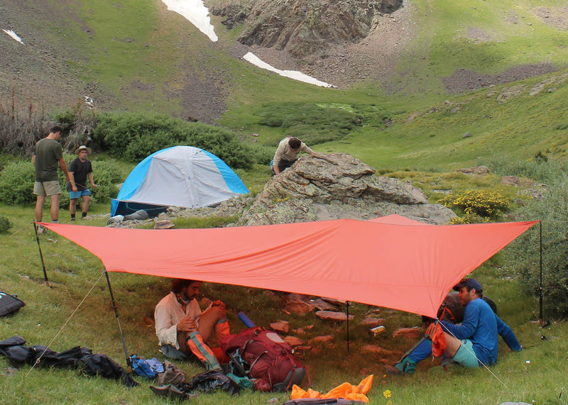 Men sitting underneath an XL Kuhli shelter in the mountains on grass.