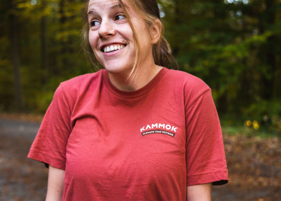 Front side of shirt, women wearing a Kammok Ride in Wonder Tee in red with a graphic of a woolly bear caterpillar and text Ride in Wonder. 
