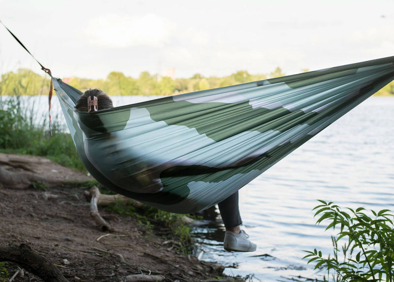 Woman swinging in a Kammok Hammock Roo Double Printed next to river.