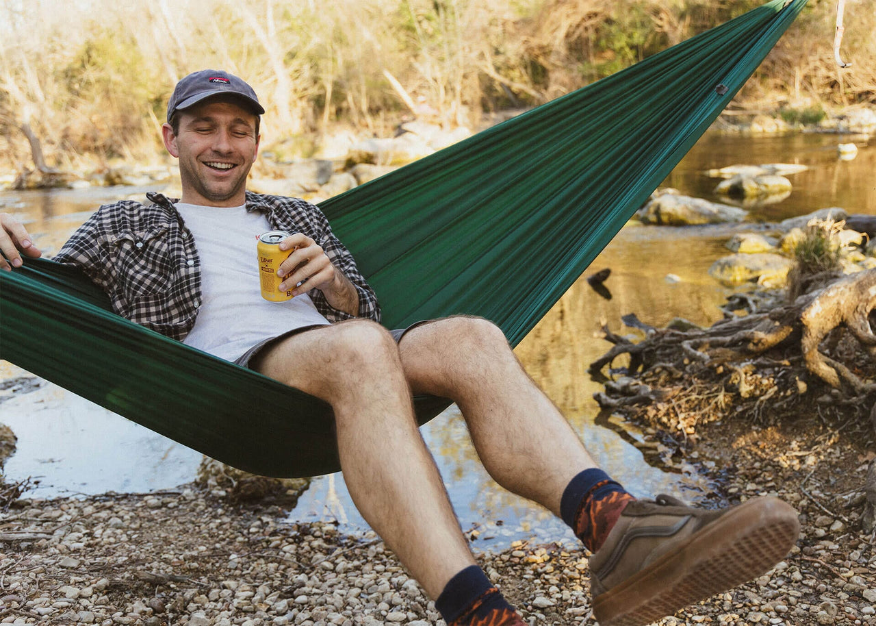 Man drinking beer while swinging in a Kammok Hammock Roo Double on the river.