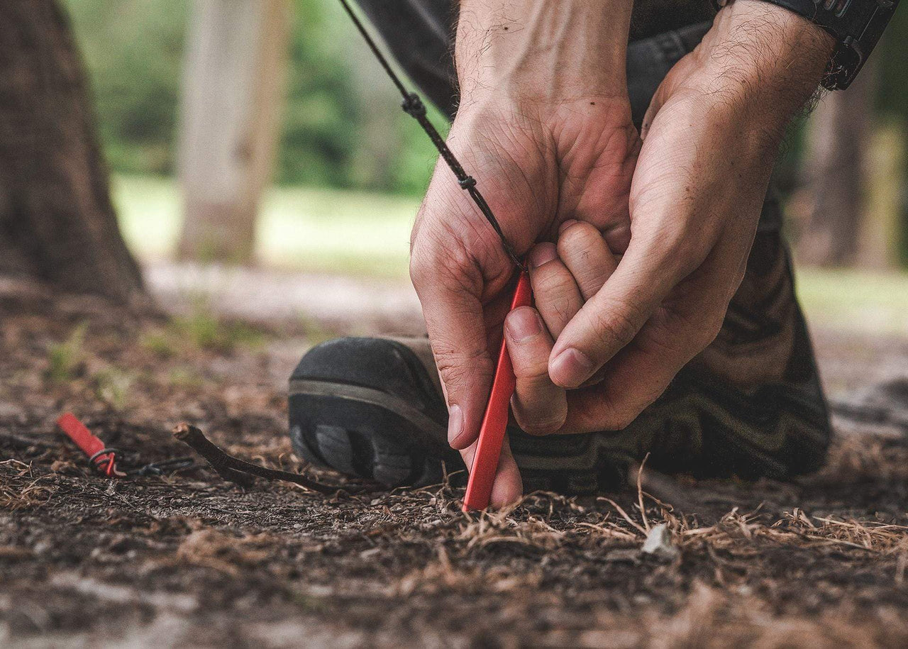 Close up of man's hands putting a Kammok stake in the ground.