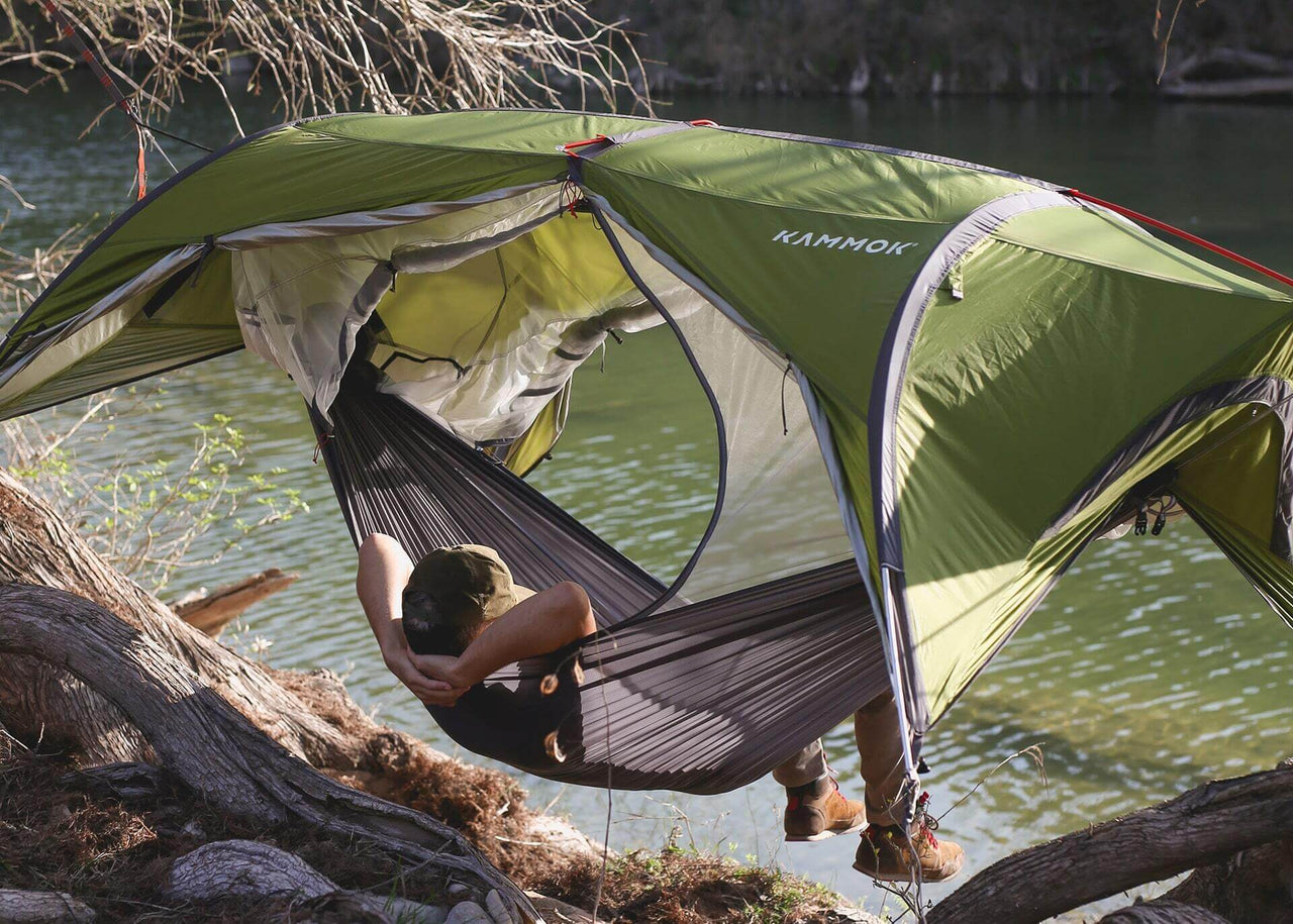 Man lounging in a Sunda hammock tent overlooking the water.