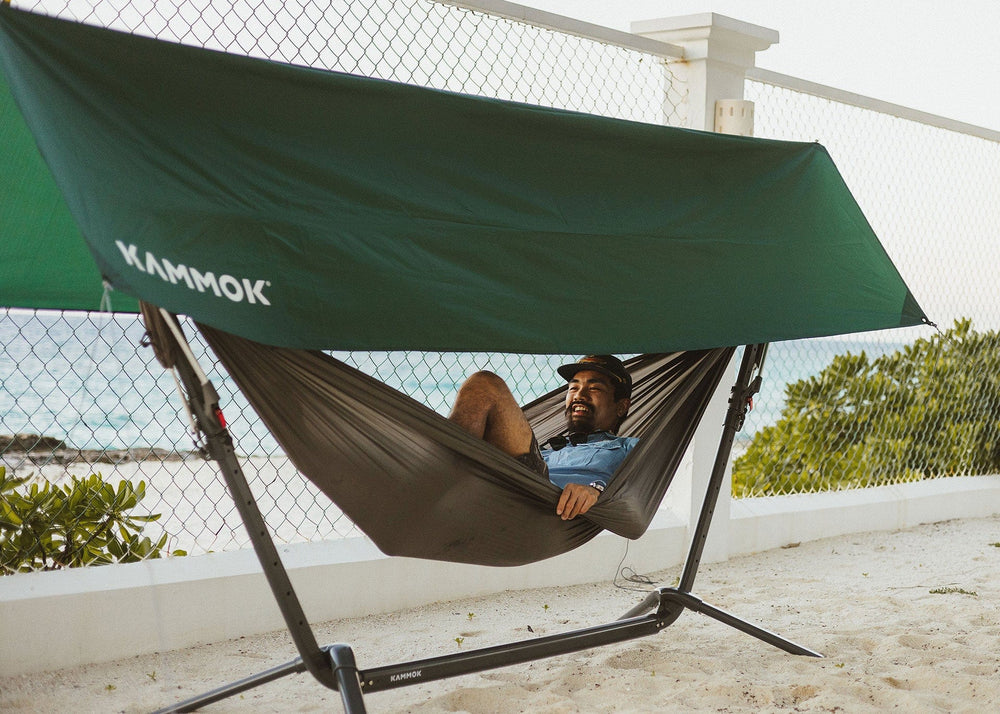 Man sitting in Swiftlet hammock stand with Roo Double shaded by Swiftlet Shade Kit on the beach.