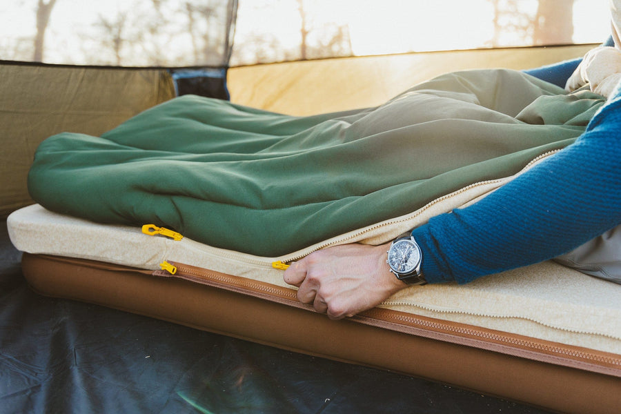 Man zipping the Ursa Sleep System Camp Comforter to the Memory Foam topper.