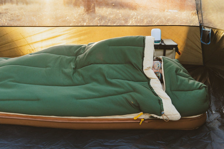 Man laying down in the Kammok Ursa Sleep System with the attached hood over his head, tucked into bed inside of a tent.
