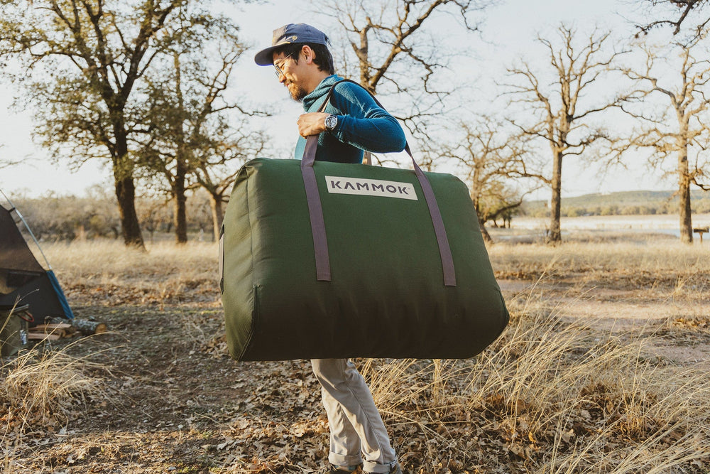Man carrying the Kammok Ursa Sleep System in the travel case at camp.