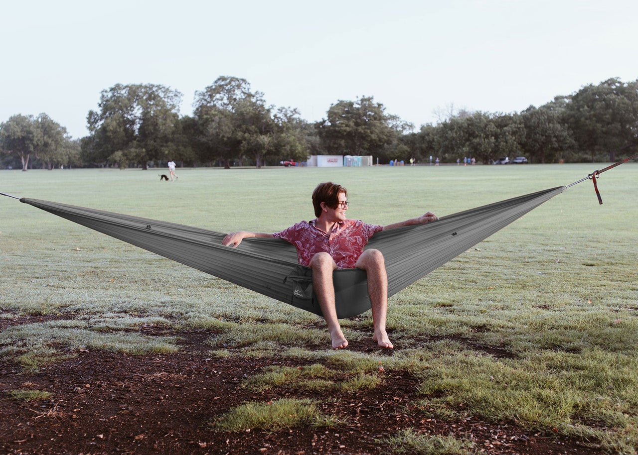 Sitting outside at a part on a Kammok Hammock Roo Double XL Granite Gray strung between two trees.